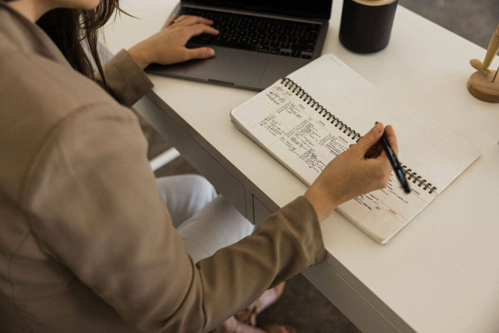 Woman writing in notebook with laptop